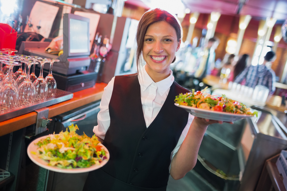 Pretty barmaid holding plates of salads in a bar